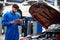 Mechanic in blue workwear uniform holding tablet and check something with blur lifted car in the background. Automobile repairing