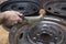 Mechanic cleans the steel wheel rim manually with a wire brush.