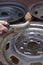 Mechanic cleans the steel wheel rim manually with a wire brush.