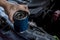 A mechanic holding an old oil filter removed from a SUV. Placed on top of an open hood of the vehicle