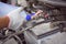 Mechanic man pouring distilled water to fill car battery in automobile engine at repair service workshop garage, close up