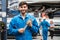 Mechanic standing and hold a wrench with blur his assistant talking with customers in the background. Auto car repair service.