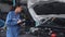 Mechanic woman holding clipboard while examining engine of car in the garage.