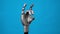 A mechanical hand flexes its fingers and shows a rock sign. Gray cyborg arm on a blue background.