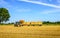 Mechanized loading of straw bales on flat farm trailers