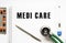 MEDI CARE is written in a notebook on a white table next to pills and a stethoscope