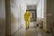 A medic or doctor in a yellow suit of bacterial and chemical protection walks along the corridor of an old hospital