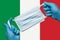 Medic holding respiratory face mask in hands in blue gloves on background flag of Italy or Italian Tricolour. Concept