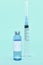 Medical ampoule (vial) with vaccine and syringe on light blue background. White label on bottle. COVID-19 vaccine vial