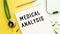 MEDICAL ANALYSIS is written in a notebook on a color table next to pills and a stethoscope