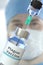 Medical bottle with plague vaccine and syringe against blurred doctor`s face, 3D rendering