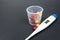 Medical capsules, tablets and clinical thermometer inside measuring cup on black background