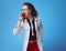 Medical doctor woman biting apple with stuck syringe on blue