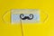 Medical face mask, paper black mustache on a stick on bright yellow background, close-up. Celebrating April Fools ` Day during th