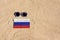 A medical mask in the color of the Russia flag lies on the sandy beach next to the glasses.