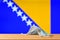 A medical mask lies on the table against the background of the flag of Bosnia and Herzegovina.