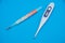 The medical mercury thermometer and electronic thermometer lie over light blue background.