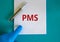 Medical and PMS, premenstrual syndrome symbol. Pen. White note with the word `PMS`. Beautiful blue background. Doctor hand in bl
