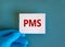 Medical and PMS, premenstrual syndrome symbol. White card with the word `PMS`. Beautiful blue background. Doctor hand in blue