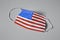 Medical protective mask with USA flag pattern on grey background, top view. Dangerous virus