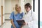 Medical staff analyzing report and working at clinic. Senior caucasian doctor having discussion in a hospital hallway with nurse.