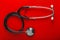 Medical stethoscope is black with metal parts on a clean red background. Layout for the designer
