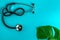 A medical stethoscope and a large green leaf of a monstera plant on an aquamarine background.