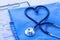 Medical stethoscope twisted in heart shape lying on patient medical history list and blue doctor uniform closeup