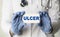 A medical worker in gloves holds a card with the words ULCER. Medical concept