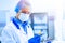 A medical worker, a laboratory assistant in a protective mask, visor, disposable cap and rubber gloves stands in a laboratory,