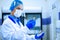 A medical worker, a laboratory assistant in a protective mask, visor, disposable cap and rubber gloves stands in a laboratory,