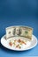 Medicines costs money. Drugs and dollars.White plate with multi-colored pills and capsules and a 100 dollar bill on a