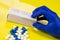 Medicines and pills on yellow background next to pill box held by hand wearing hospital gloves