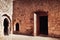 Medieval door in stone courtyard under scorching sun with monk in gray cloak.