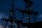 Medieval old wooden ship dark mast and sails silhouette at night twilight time on cloudy sky background with many hanging lamps