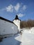 Medieval tower of monastery in snowed hills near the river bank under blue cloudy sky