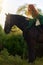 Medieval woman princess in green dress sits astride black steed horse.