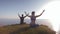 Meditating together, young man and woman in sunlight sitting in lotus position on land on top of mountain looking at sea