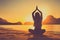 Meditating woman by the ocean with rocks in the background at sunset