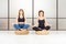 Meditating women sitting in the lotus pose with closed eyes in the white room. It`s yoga time.