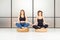 Meditating women sitting in the lotus pose with closed eyes in the white room. It`s yoga time.