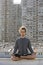 Meditating young european man sitting with eyes closed in lotus pose on blurry urban residential building. Yoga concept