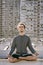 Meditating young european man sitting with eyes closed in lotus pose on blurry urban residential building. Yoga concept