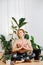 Meditating young woman sitting in easy pose, surrounded by potted plant