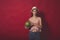 Meditative girl with pink make up, wearing jeans, hat and top, posing at red studio background, holding watermelon, emotionally