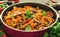 Mediterranean eggplant pasta in pot with tomatoes, pepper and parsley on grey background.