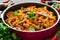 Mediterranean eggplant pasta in pot with tomatoes, pepper and parsley on grey background.