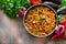 Mediterranean eggplant pasta in pot with tomatoes, red pepper and parsley on grey background.