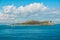 Mediterranean island framed under clouds with boats passing by.