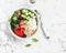 Mediterranean quinoa bowl with avocado, cucumbers, olives, roasted pepper, feta cheese, arugula. On a white background.